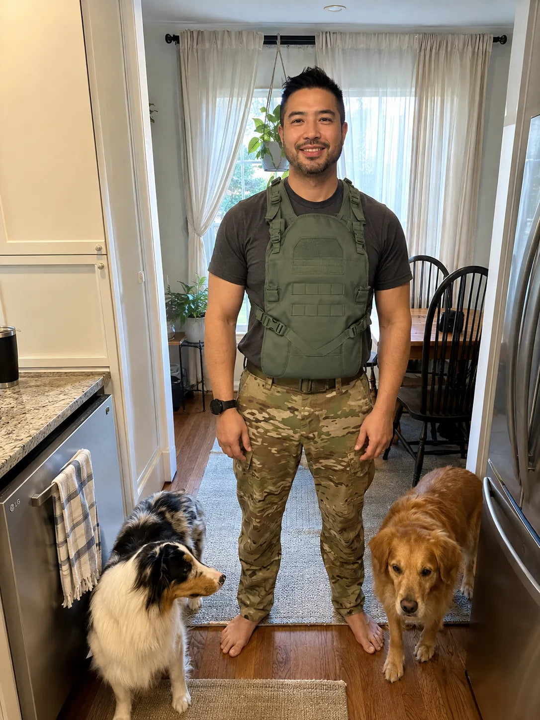 Padre en su cocina con dos perros, con el Tactical Baby Carrier Ranger Green